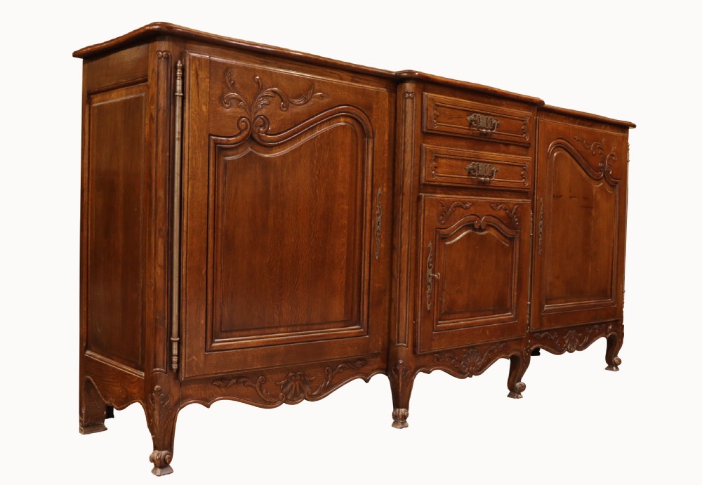A French Louis XV style warm brown oak sideboard featuring three carved panel doors, two central drawers, brass hardware, and cabriole feet. View VI