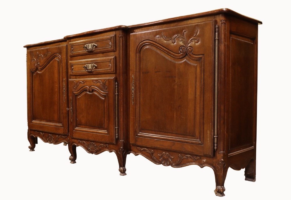 A French Louis XV style warm brown oak sideboard featuring three carved panel doors, two central drawers, brass hardware, and cabriole feet. View VII