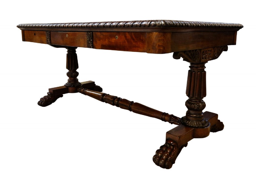 A George IV mahogany partners writing table featuring a patterned top edge, three frieze drawers, carved pedestal supports, a turned stretcher, and claw feet. View IV