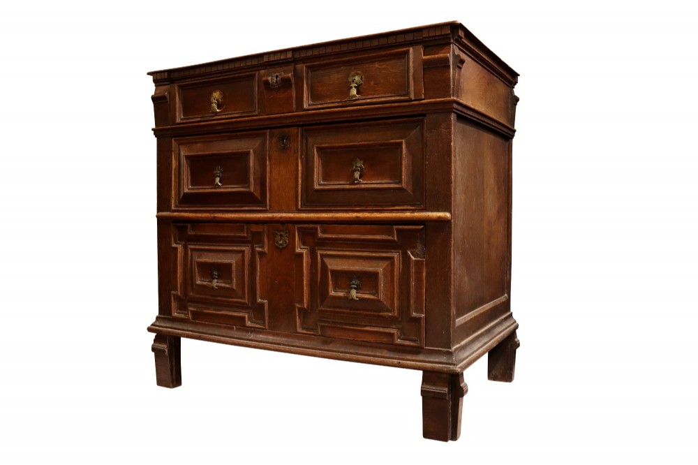 A Charles II dark oak chest of drawers featuring deep geometric mitred mouldings on the drawer fronts and brass drop handles. View IV