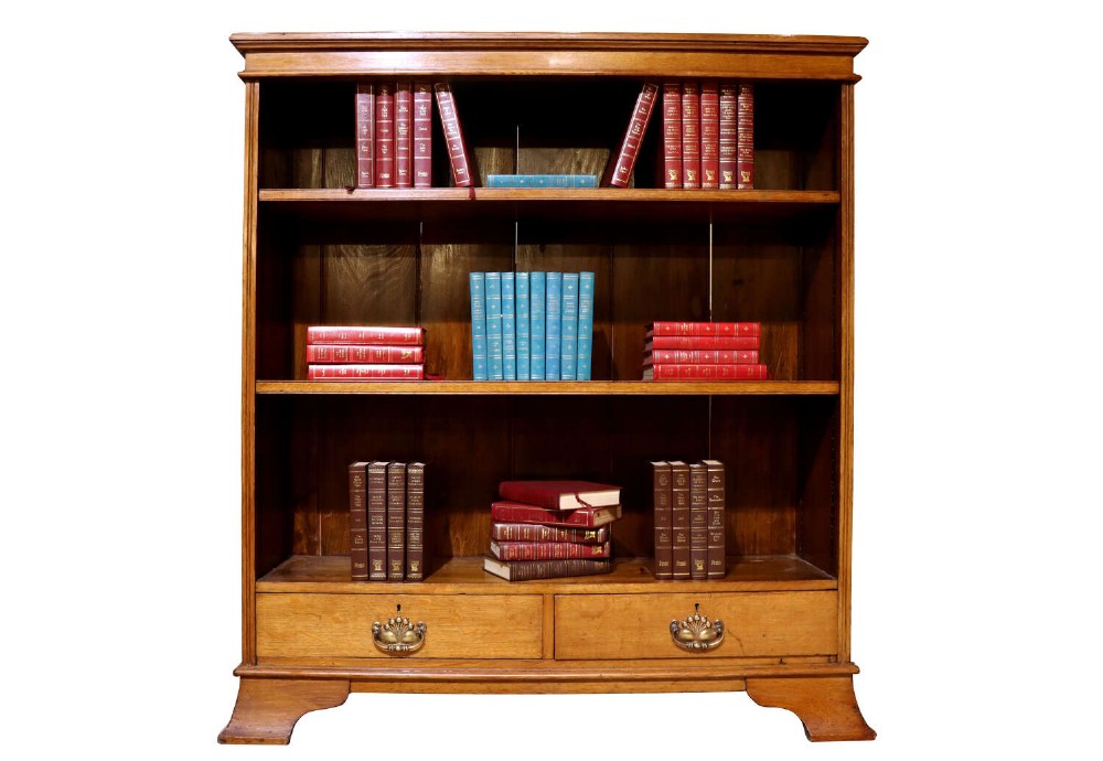 Late 19th-century open oak bookcase featuring three tiers of shelving, two lower drawers with brass drop handles, and a moulded top cornice.