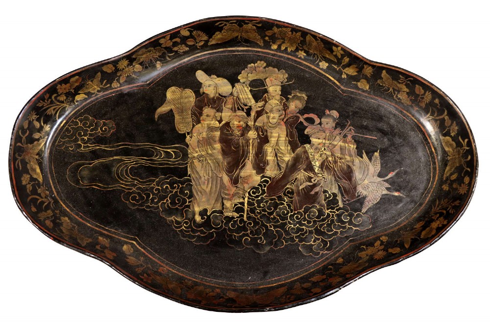 An oval black lacquered tray featuring gilt Chinoiserie decoration of figures on clouds surrounded by a floral border.