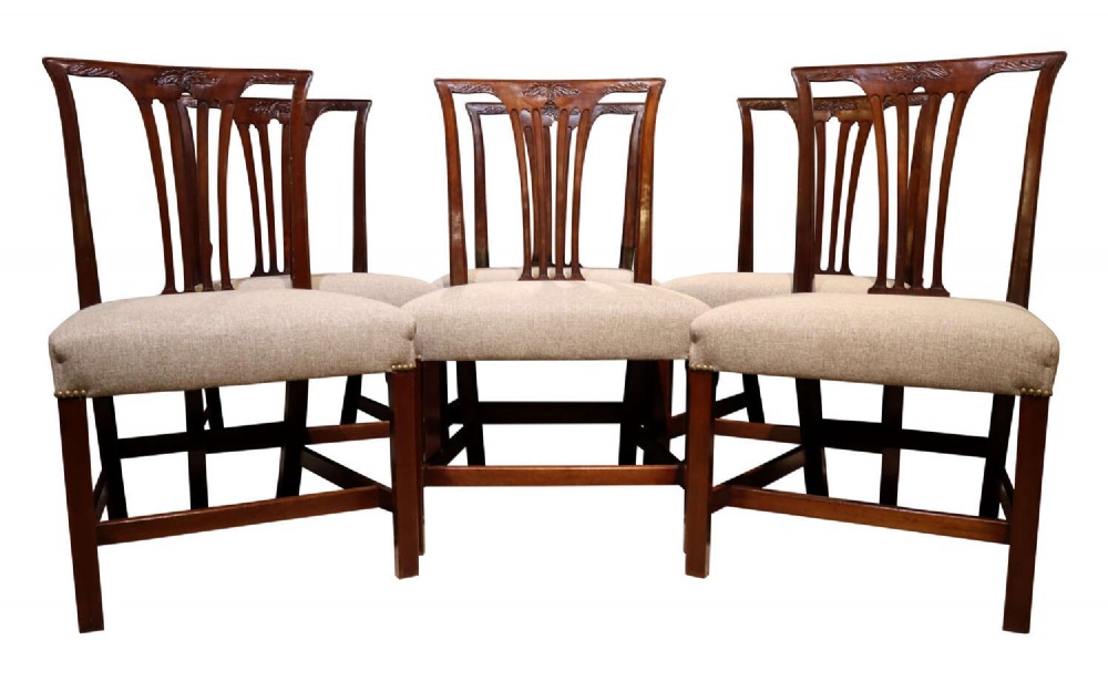 A set of six Georgian mahogany dining chairs featuring carved crest rails, vertical back splats, square legs with stretchers, and beige upholstered seats.