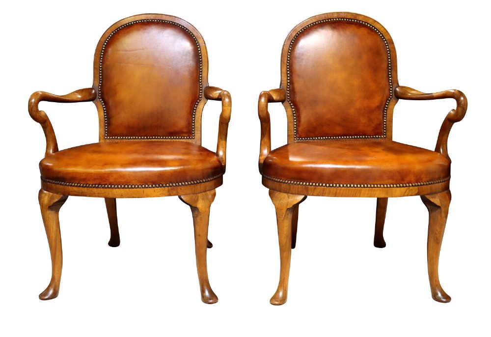 A pair of early twentieth-century walnut armchairs featuring warm tan leather upholstery with brass studding and cabriole legs.