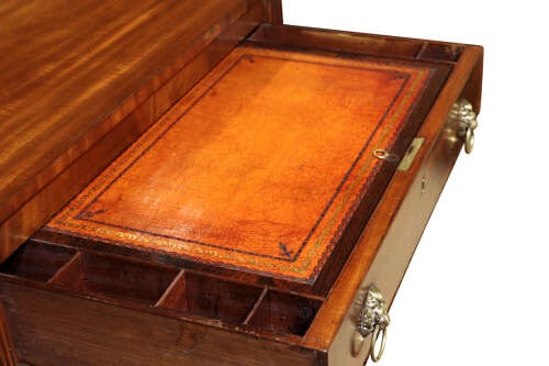 A Regency mahogany writing table with two drawers featuring brass lion-mask ring handles and reeded legs on brass castors. View V