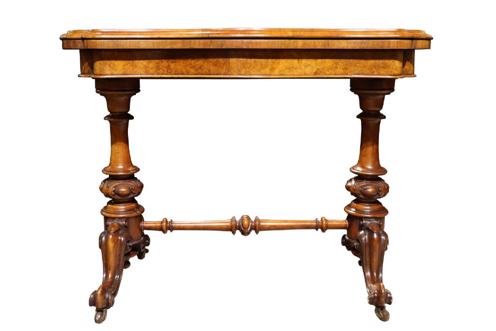 A Victorian burr walnut card table with a fold-over swivel top, carved twin pedestal supports, turned stretcher, and splayed legs on castors.