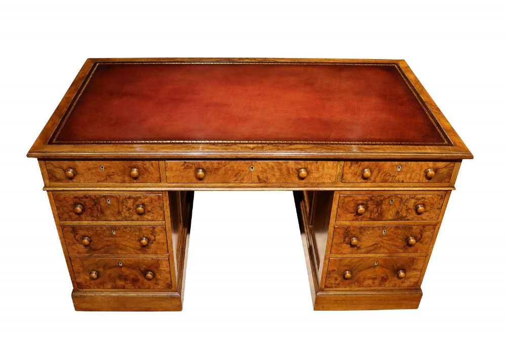 A Victorian burr walnut pedestal desk featuring nine drawers with turned wooden knobs and a red leather gilt-tooled writing surface.