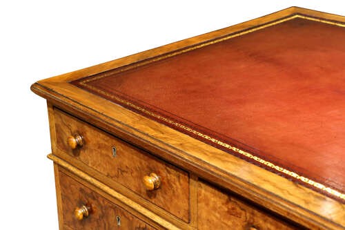A Victorian burr walnut pedestal desk featuring nine drawers with turned wooden knobs and a red leather gilt-tooled writing surface. View VI