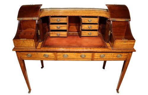An Edwardian satinwood Carlton House desk featuring a curved top gallery with small drawers, marquetry inlay, a leather writing surface, and tapered legs on brass castors. View II