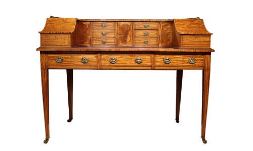 An Edwardian satinwood Carlton House desk featuring a curved top gallery with small drawers, marquetry inlay, a leather writing surface, and tapered legs on brass castors. View III