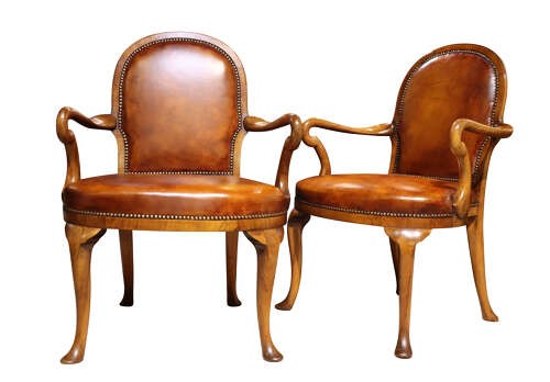 A pair of early twentieth-century walnut armchairs featuring warm tan leather upholstery with brass studding and cabriole legs. View VII