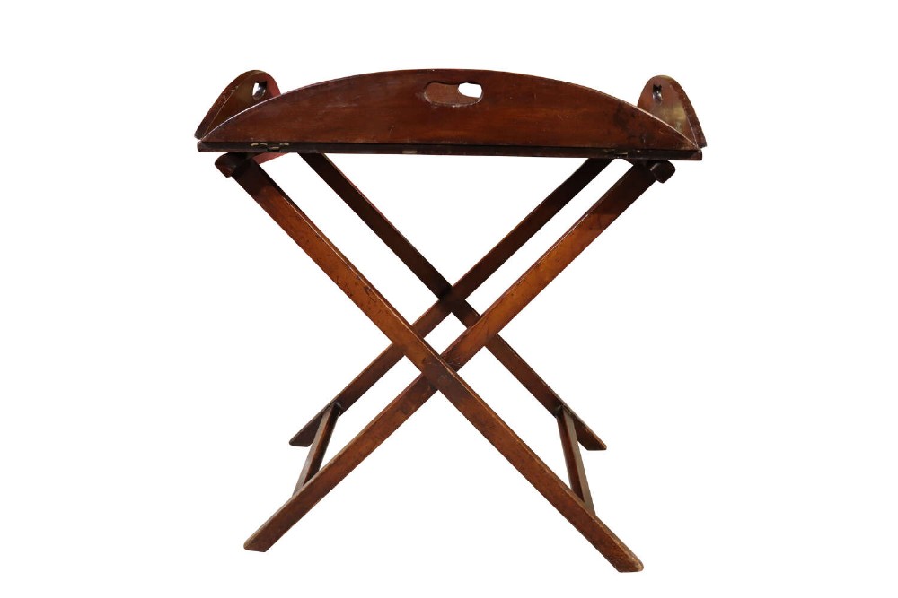 A William IV mahogany butlers tray with carved cutout handles situated on an X-frame folding wooden stand.