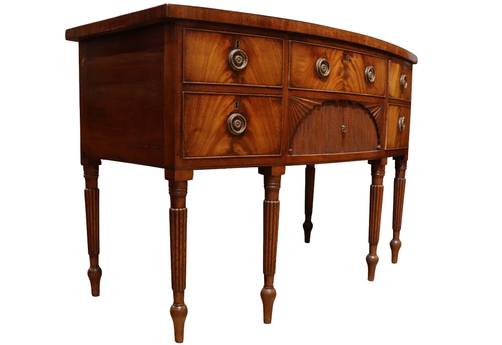 A Regency mahogany bow-fronted sideboard featuring a central drawer with tambour cupboard below, flanked by drawers and supported on six turned, fluted legs. View II