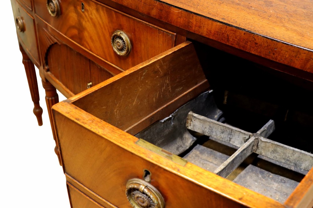 A Regency mahogany bow-fronted sideboard featuring a central drawer with tambour cupboard below, flanked by drawers and supported on six turned, fluted legs. View V