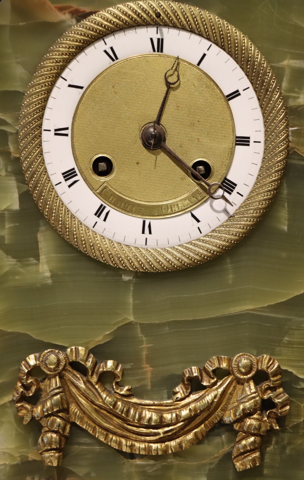 An early nineteenth-century French mantel clock constructed from polished green onyx with an arched case, gilt-bronze ribbon swag mount, and a central dial with Roman numerals. View III
