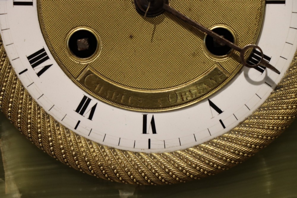 An early nineteenth-century French mantel clock constructed from polished green onyx with an arched case, gilt-bronze ribbon swag mount, and a central dial with Roman numerals. View VI