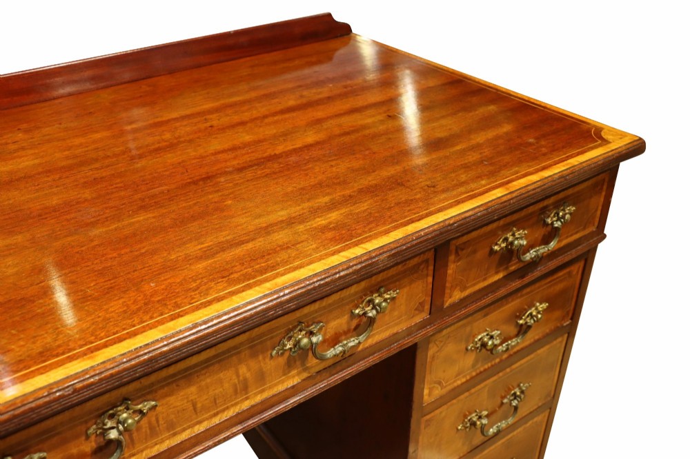 A late Victorian mahogany pedestal desk with satinwood stringing inlay, nine drawers, and brass handles. View V