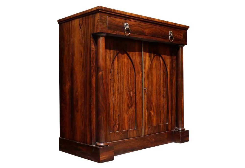 A Regency period rosewood chiffonier featuring two Gothic arched panel doors flanked by turned columns and topped with a single drawer with twin brass lion-head ring handles. View II