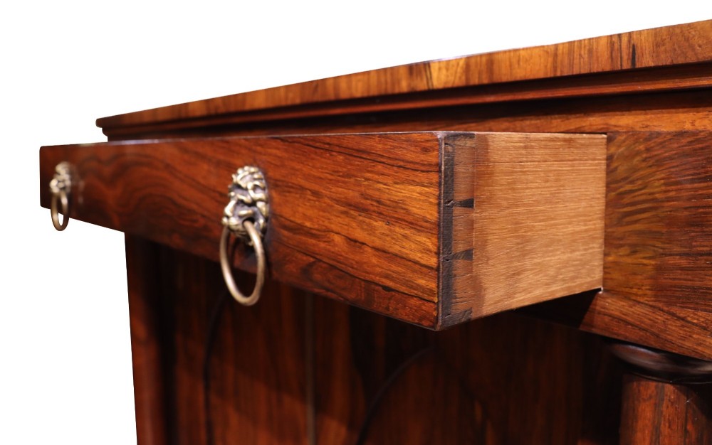 A Regency period rosewood chiffonier featuring two Gothic arched panel doors flanked by turned columns and topped with a single drawer with twin brass lion-head ring handles. View VII