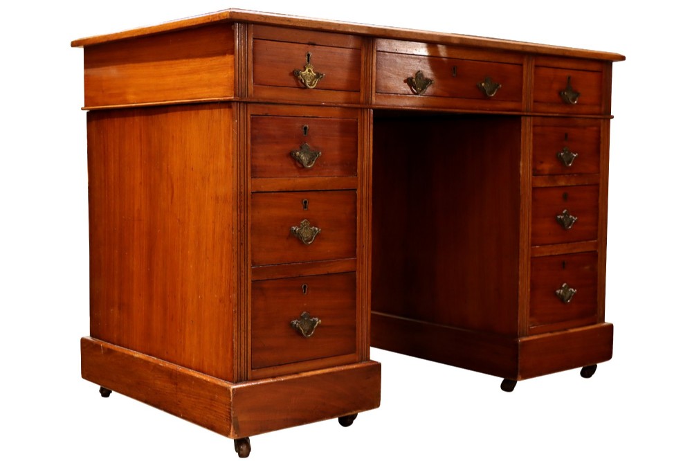 A small Edwardian walnut pedestal desk featuring a green leather top with gold tooling, nine brass-handled drawers, fluted side details, and castors at the base. View II