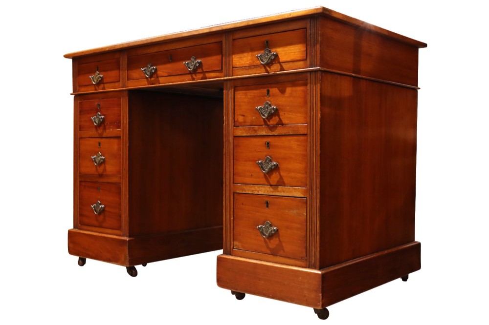 A small Edwardian walnut pedestal desk featuring a green leather top with gold tooling, nine brass-handled drawers, fluted side details, and castors at the base. View IV