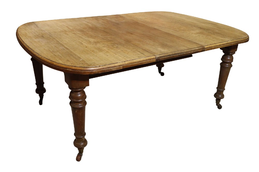 A Victorian oak extending dining table featuring rounded D-ends, a removable centre leaf, and four turned legs on brass castors.