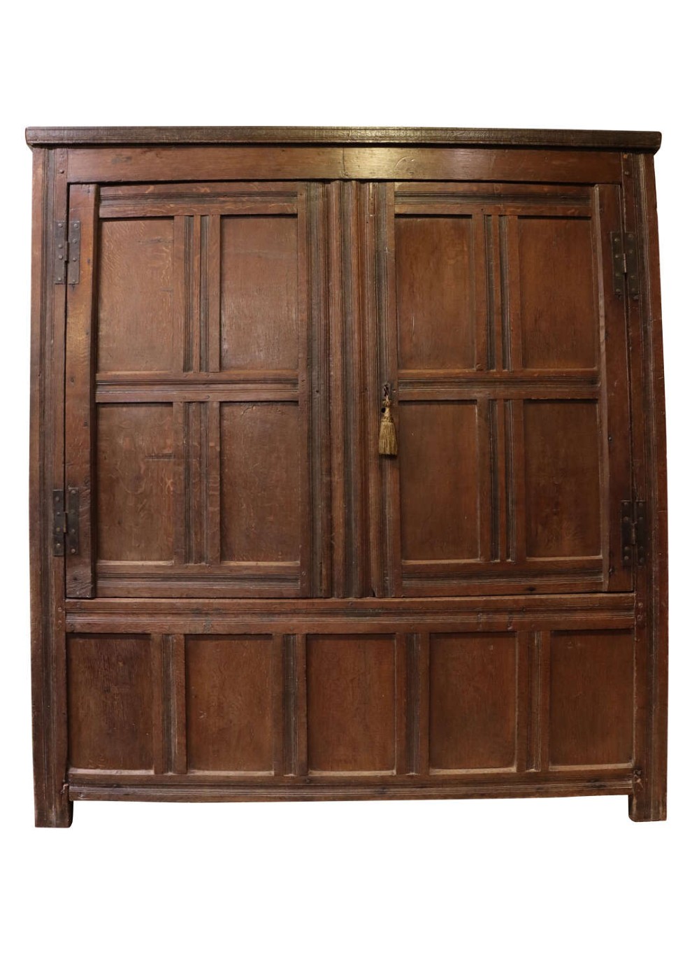 A seventeenth-century dark oak vestment cupboard featuring twin panelled doors with iron hinges above a lower panelled base.