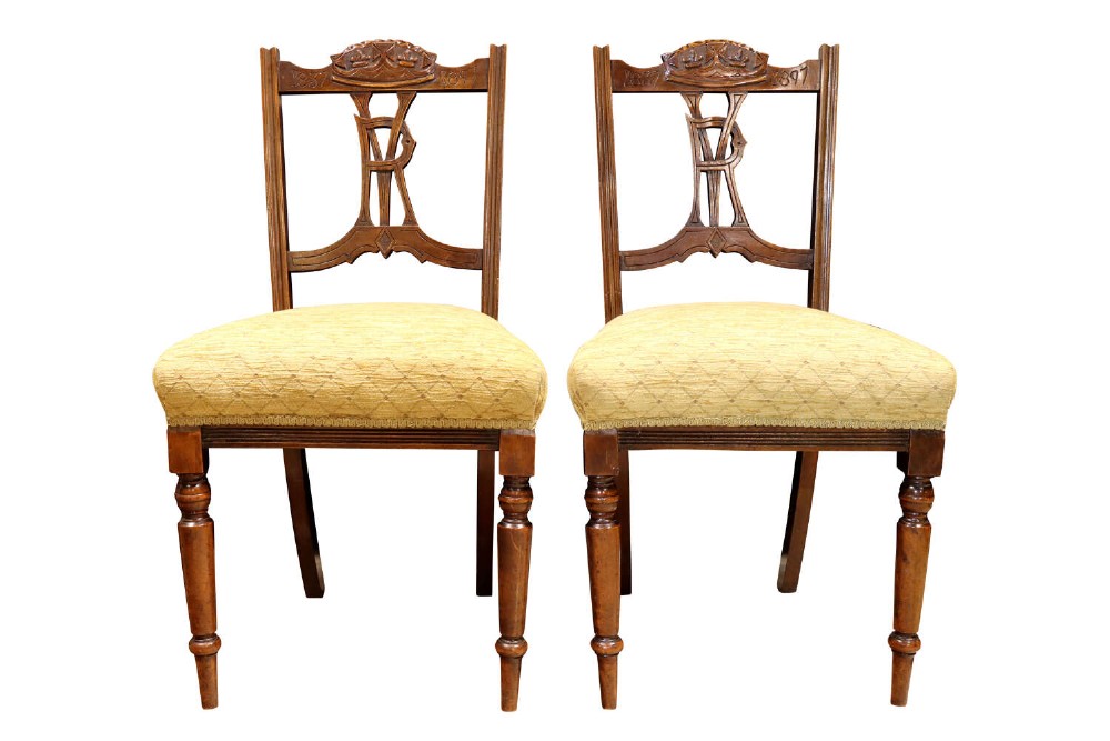 A pair of Victorian carved walnut side chairs with openwork backrests displaying a carved royal crown and monogram, resting on turned front legs with upholstered seats.
