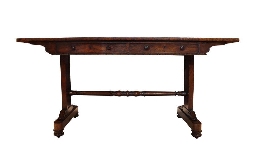 A William IV rosewood library table featuring a rectangular top, two frieze drawers with turned wooden knobs, trestle end supports, and a central turned stretcher.