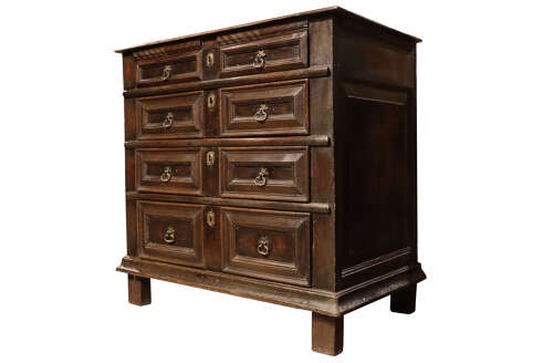 A dark oak Charles II chest of drawers featuring geometric panelled fronts, brass teardrop handles, and keyhole escutcheons. View IV