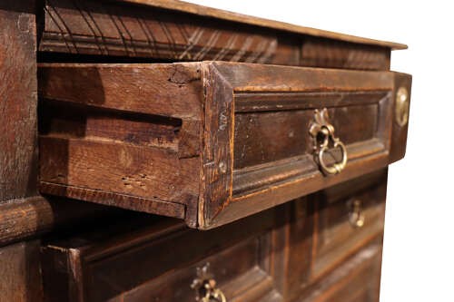 A dark oak Charles II chest of drawers featuring geometric panelled fronts, brass teardrop handles, and keyhole escutcheons. View V