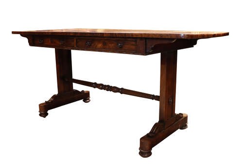 A William IV rosewood library table featuring a rectangular top, two frieze drawers with turned wooden knobs, trestle end supports, and a central turned stretcher. View III