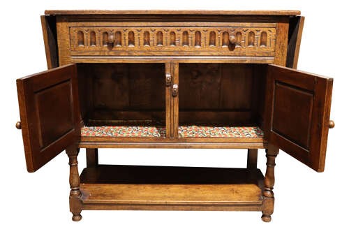 A warm brown carved oak side cabinet featuring drop-leaf top extensions, arcaded carved cupboard doors, turned legs, and a lower pot board shelf. View VI