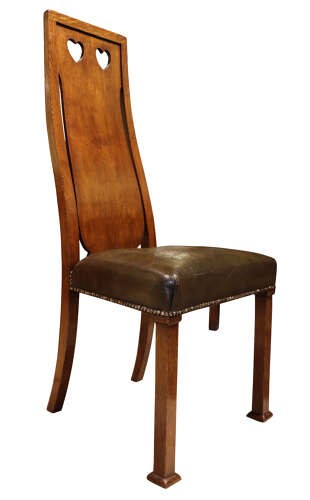 A set of six Arts and Crafts solid oak dining chairs featuring tall backsplats with heart-shaped cutouts and green leather seats with brass studding. View VI