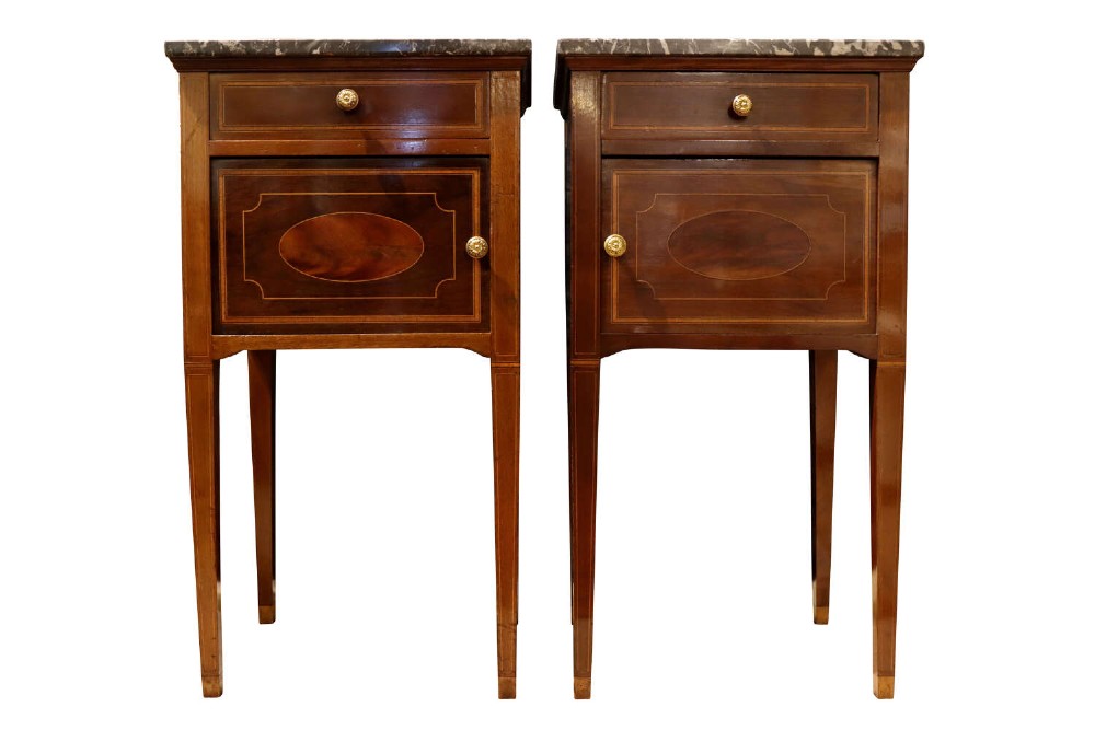 Pair of tall, slender mahogany bedside cupboards with satinwood oval inlay, dark marble tops, single drawers, and square tapered legs.