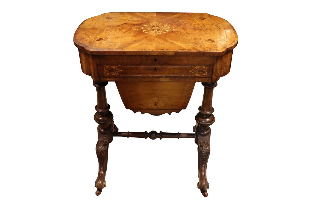 A Victorian burr walnut sewing table featuring intricate marquetry inlay on top, turned legs with carved feet, and a drop-down sewing well beneath a single drawer.