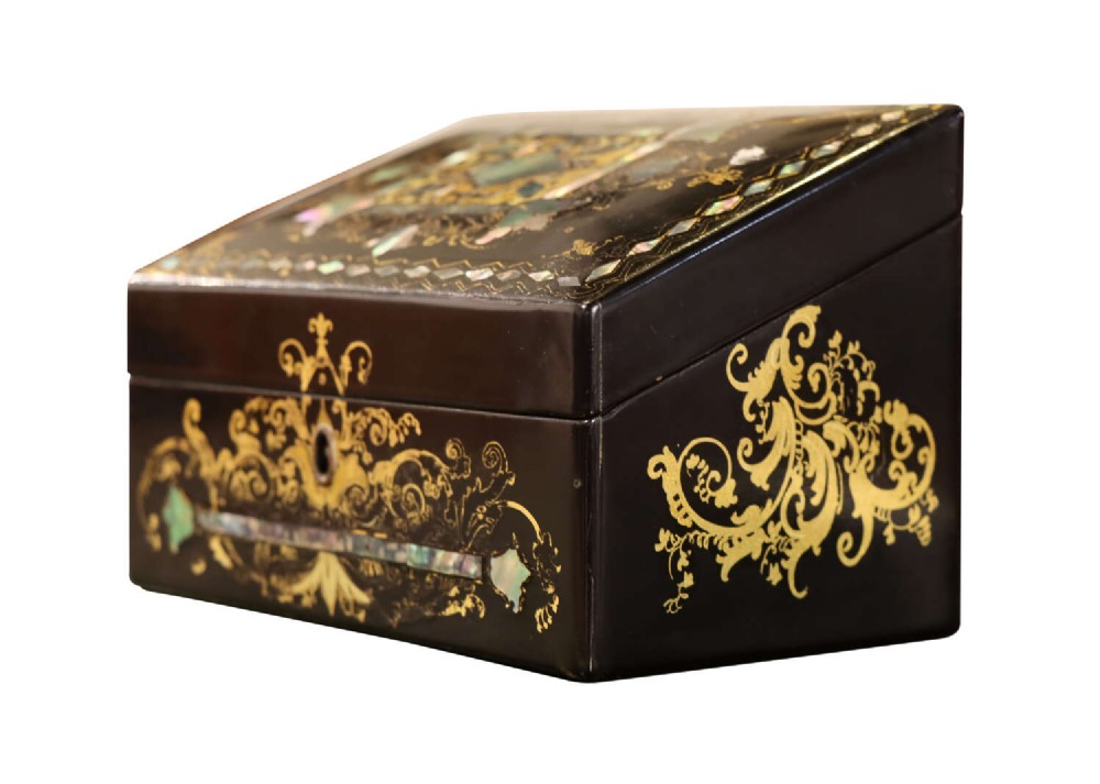 A black lacquered Victorian sloped stationery box adorned with gold leaf scrollwork and mother-of-pearl inlay.