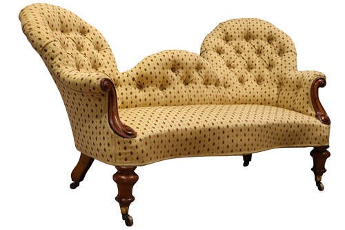 A Victorian mahogany double-ended settee featuring deep-buttoned patterned yellow upholstery, carved scroll arms, and turned legs with brass castors. View IV
