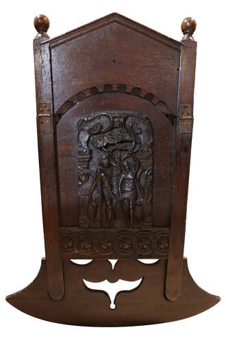 A dark carved oak rocking cradle featuring a hooded top with turned spindles, carved relief side panels, and curved rockers at the base. View V