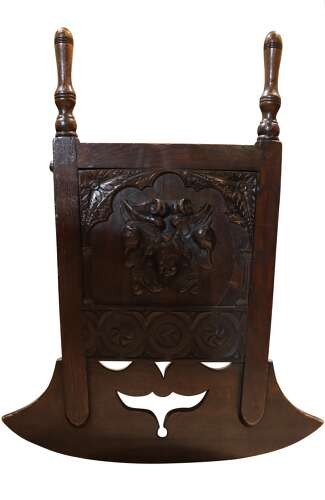 A dark carved oak rocking cradle featuring a hooded top with turned spindles, carved relief side panels, and curved rockers at the base. View IX