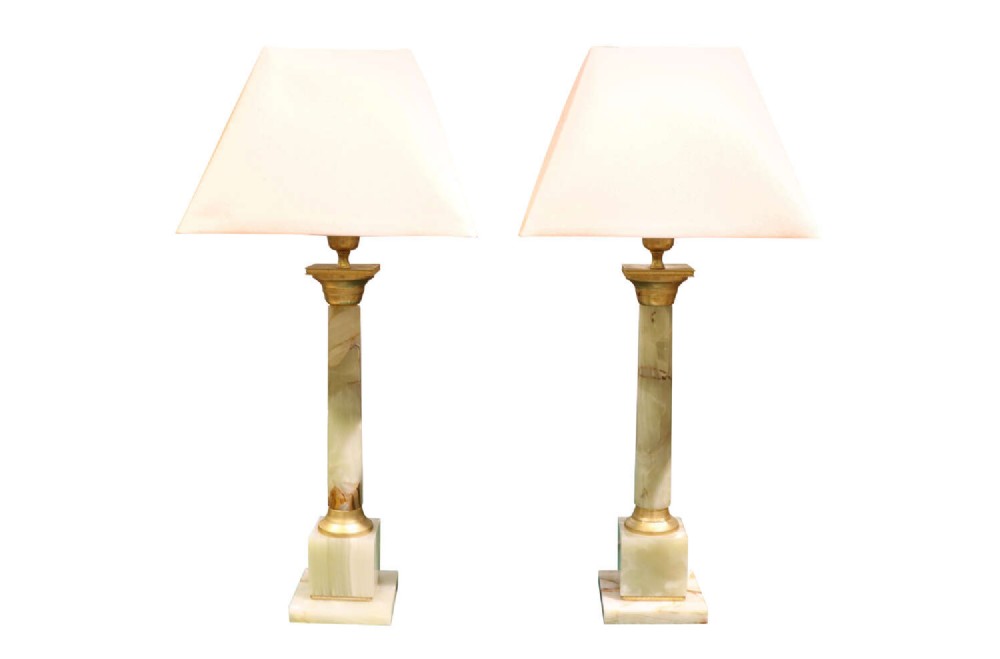 A pair of Neoclassical style table lamps featuring pale green onyx columns mounted with gilt metal capitals and bases, topped with square white lampshades.