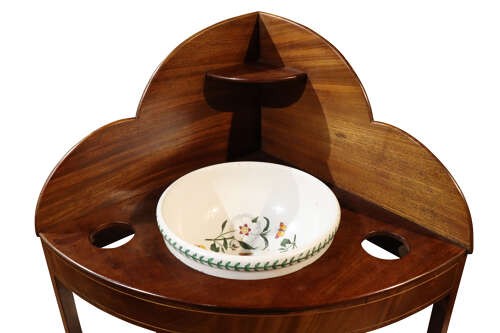 A George IV mahogany corner washstand featuring a stepped splashback with a corner shelf, stringing inlay, curved drawers, and splayed legs. View IV