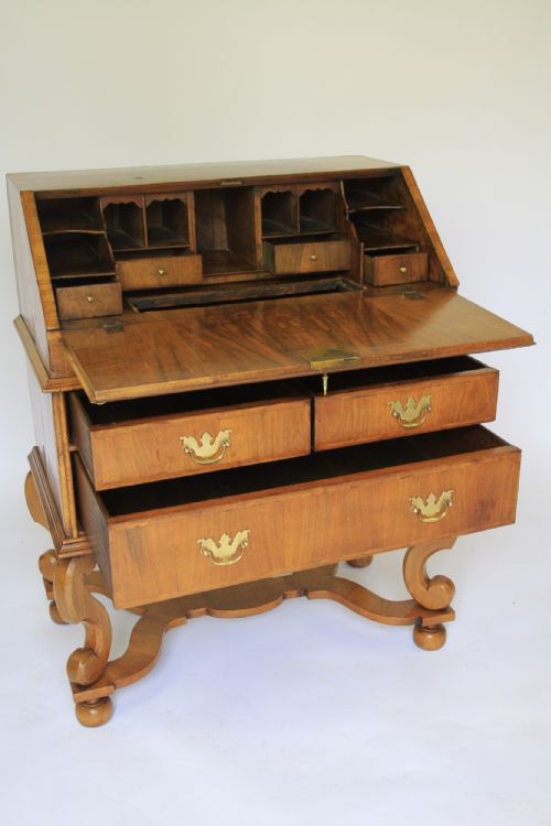 fig 1. A William and Mary Revival walnut slant-front writing bureau with brass handles and carved scroll legs connected by a shaped stretcher.