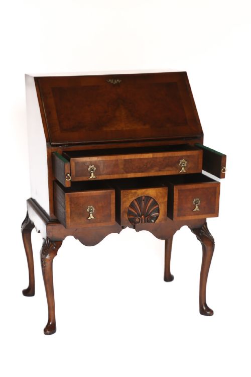 fig 1. A Georgian style walnut slant-front bureau featuring a hinged writing flap, drawers with brass handles, carved shell details, and cabriole legs.
