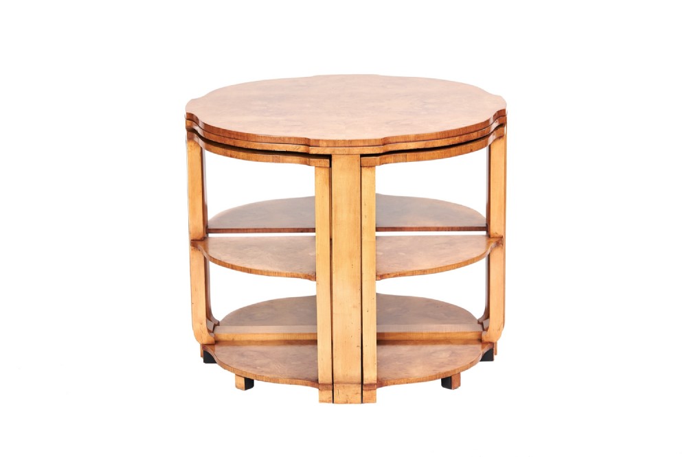 A circular Art Deco nest of four burr walnut tables featuring scalloped edges and fitted lower shelves.