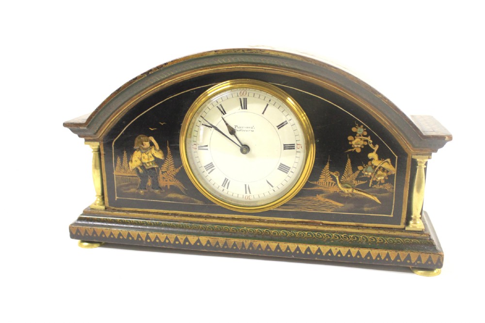 A 1920s arched black lacquered mantel clock decorated with gilded chinoiserie scenes, turned brass columns, and a cream dial with Roman numerals.