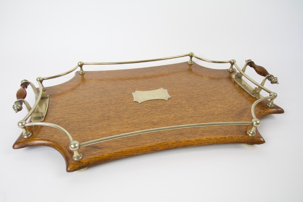 An antique shaped oak serving tray featuring a metal gallery rail, side handles with turned wooden grips, and a central metal cartouche.