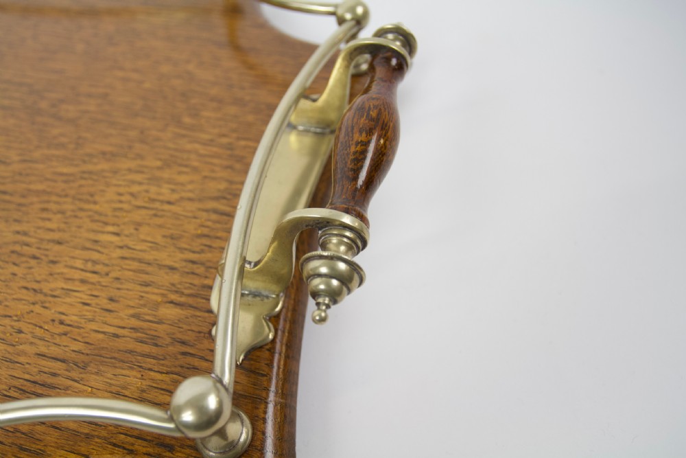 An antique shaped oak serving tray featuring a metal gallery rail, side handles with turned wooden grips, and a central metal cartouche. View VI