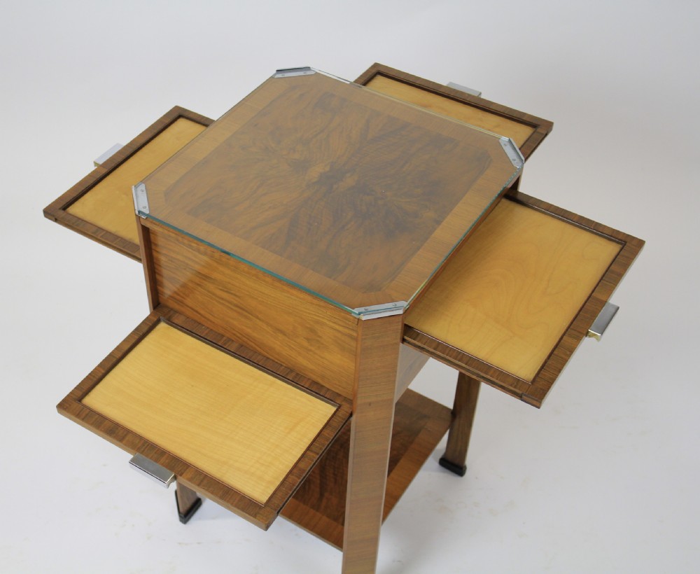 An Art Deco two-tier walnut side table featuring a square glass top, chrome corner grips, a lower shelf, and four pull-out maple slides extending from each side.