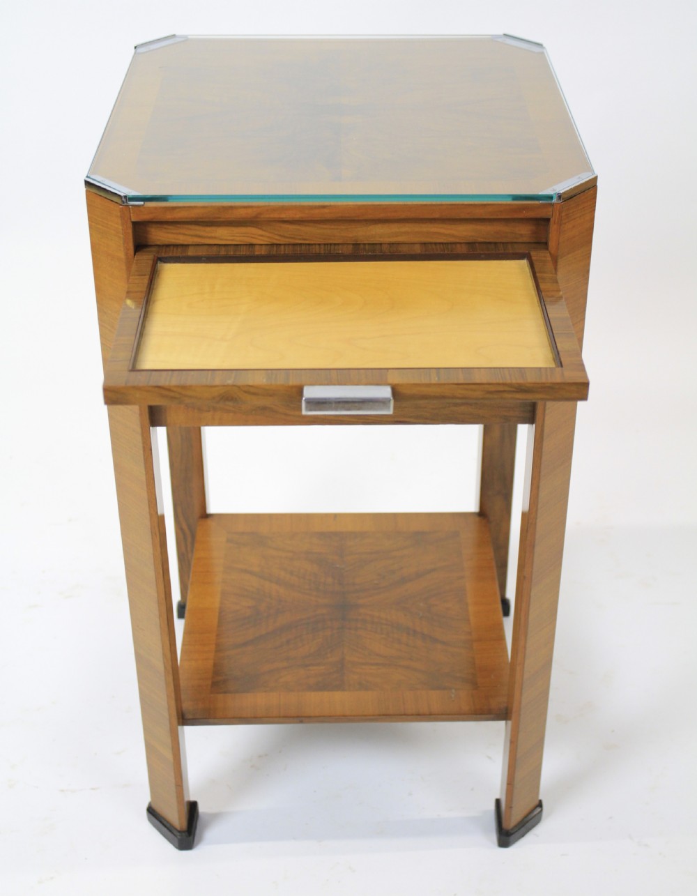 An Art Deco two-tier walnut side table featuring a square glass top, chrome corner grips, a lower shelf, and four pull-out maple slides extending from each side. View VII